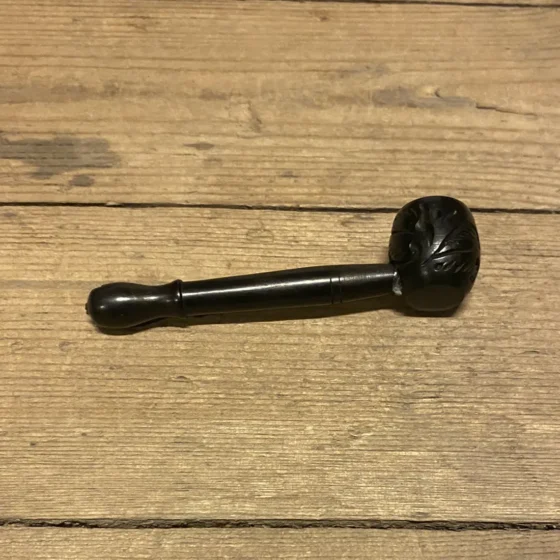 En sort træpibe med en glat overflade præsenterer sig med en enkel, elegant form. Munden er let buet, og stammerne er slanke med en naturlig finish, der fremhæver træets struktur. Piben har en bred åbning, der er omgivet af en tynd metalring, hvilket tilføjer en kontrastfuld detalje til det overordnede design.