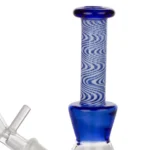En blå glasbong står oprejst med en glat, cylindrisk form. Den har en gennemsigtig bund og en opadgående hals, der forsynes med en krumning, hvilket skaber en elegant silhuet. Overfladen er blank og reflekterer lys, mens der er en rund åbning til indførsel af røg. Det samlede design er minimalistisk og strømlinet.