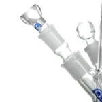 En isbong i klart glas, der måler 50 cm i højden. Den har en cylindrisk form med en bred base og en slank hals. Nederst er der et stort kammer med en iskerne, mens en rørformet mundstykke er placeret øverst. En skål til urter er integreret i siden, og der er detaljerede fordybninger og teksturer på overfladen, der skaber et interessant visuelt indtryk.