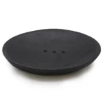 En oval sæbeskål i sort, fremstillet af flodsten, præsenterer en glat overflade med naturlige variationer i nuancerne. Skålen har en let buet form, der fremhæver dens organiske design. Kanten er diskret, og der ses subtile teksturer, der tilføjer karakter. Den sorte farve giver et elegant og tidløst udtryk, ideel til moderne badeværelsesindretning.
