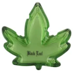 Asken er lavet af klart glas med en rund form og en let hævet kant. Den har en dyb grå sort farve, der minder om cannabisbladets nuancer, og er dekoreret med detaljerede blade i en mørkere skygge. Overfladen er glat med en let reflekterende kvalitet, der fremhæver de indviklede mønstre i designet.