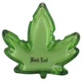 Asken er lavet af klart glas med en rund form og en let hævet kant. Den har en dyb grå sort farve, der minder om cannabisbladets nuancer, og er dekoreret med detaljerede blade i en mørkere skygge. Overfladen er glat med en let reflekterende kvalitet, der fremhæver de indviklede mønstre i designet.