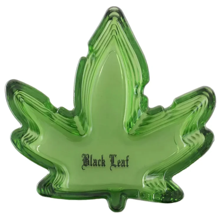 Asken er lavet af klart glas med en rund form og en let hævet kant. Den har en dyb grå sort farve, der minder om cannabisbladets nuancer, og er dekoreret med detaljerede blade i en mørkere skygge. Overfladen er glat med en let reflekterende kvalitet, der fremhæver de indviklede mønstre i designet.
