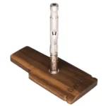 En træstander med en glat, naturlig finish, der præsenterer en dyb, varm brun farve. Standens design inkluderer en cirkulær base med en let hævet kant og en indvendig udskæring, der holder en metalcap sikkert på plads. Overfladen har synlige åretegninger, der tilføjer en organisk tekstur, mens kanterne er let afrundede for et blødere udtryk.