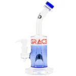 En transparent bong i klart glas, 28 cm høj, med en karakteristisk form. Den har en bred, stabil bund og en slank hals, der afsluttes med en skarp, rund åbning. Indvendigt ses en kompleks perkolator med flere små huller, der skaber bobler. Overfladen er glat, og bunden er dekoreret med et bølgemønster, der tilføjer tekstur.
