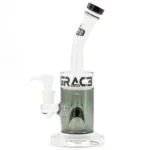 En 28 cm høj bong i røget grå glas præsenterer sig med et strømlinet design. Den har en bred, stabil base, der glider op til en slank hals, afsluttet med en buet mundstykke. Den brede åbning ved bunden indeholder et nedadgående rør med en lille skål. Overfladen har en glat tekstur med subtile nuancer og refleksioner, der fanger lyset.