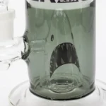 En 28 cm høj bong fremstår i en røget grå farve med et glat, gennemsigtigt glasmateriale. Den har en buet form, der afsluttes med en bred åbning for vand. Nederst er der en skål til urter, der er integreret i designet. Overfladen er glansfuld med fine detaljer og en stabil fod, der sikrer balance.
