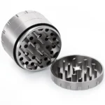 En stålgrinder med en diameter på 63 mm præsenterer en poleret, sølvfarvet overflade. Den har en cirkulær form og er opdelt i flere sektioner med skridsikre riller, der sikrer et godt greb. Indvendigt ses skarpe tænder, der er designet til at male urter. Låget har en magnetisk lukning for sikkerhed og stabilitet.