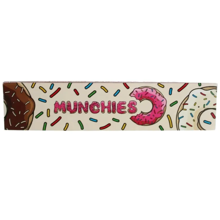 En lang, smal pakke i en mørkeblå farve med farverige illustrationer af en abe og snacks. Pakken har en mat overflade og viser et grafisk mønster med bølger og stjerner. Teksten er i hvid og gul, hvilket skaber kontrast. Øverste del af pakken er lukket med en tydelig, skarp kant.