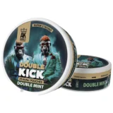 En dobbelt kick skateboard med en mintgrøn overflade prydet med sorte detaljer. Decket har en let buet form, hvilket giver en ergonomisk profil. Hjulene er i en klar, lys farve, mens akslerne fremstår i en mørkere metalfinish. Skateboardets underside har et skulpturelt design med synlige skruer og en glat tekstur, der skaber kontrast til den farverige overflade.