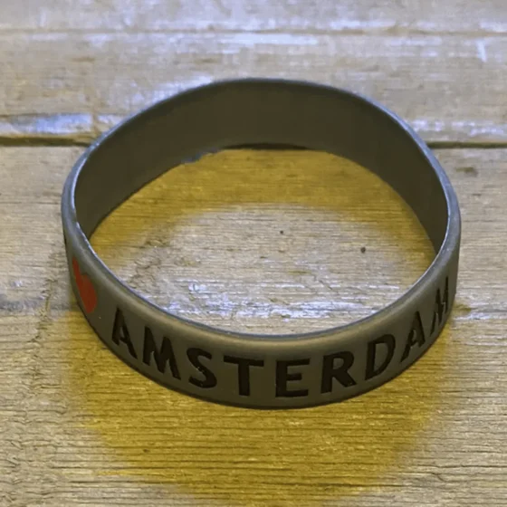 Et gråt gummiarmbånd præsenteres med en glat, ensartet overflade. Armringens form er rund med en fleksibel struktur, der muliggør tilpasning til forskellige håndledsstørrelser. Overfladen har en mat finish, hvilket skaber en subtil elegance. Armbåndet har ingen synlige mønstre eller dekorationer, hvilket understreger dets enkle design.