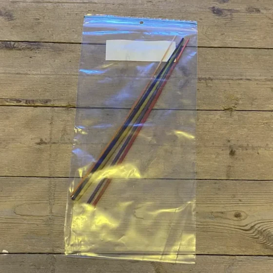 Fem pakker med røgelsespinde er arrangeret i et stramt layout. Hver pakke har en farverig, trykt etikette med forskellige mønstre og symboler. Røgelsespindene er lange og slanke, med en mørk brun farve. Etiketterne indeholder tekst, der angiver dufte og navne, og har en glat, blank overflade, der reflekterer lys.