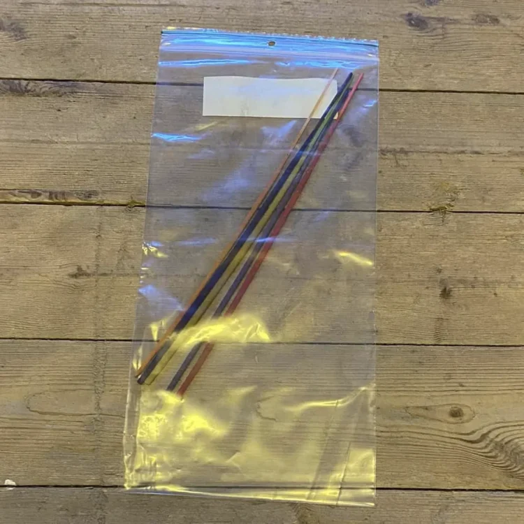 Fem pakker med røgelsespinde er arrangeret i et stramt layout. Hver pakke har en farverig, trykt etikette med forskellige mønstre og symboler. Røgelsespindene er lange og slanke, med en mørk brun farve. Etiketterne indeholder tekst, der angiver dufte og navne, og har en glat, blank overflade, der reflekterer lys.