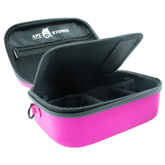 Kasse i blødt, pink materiale med en glat overflade og let skinnende finish. Foran er der et stort, hvidt logo centralt placeret, omgivet af en subtil, mørkere skygge. Kassen har afrundede hjørner og en let hævet kant, hvilket giver et moderne udtryk. Indersiden kan være opdelt i flere rum, som antyder en funktionel indretning.