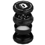 En sort hexagonal grinder med en diameter på 55 mm præsenterer sig med en matte overflade og afrundede kanter. Grinderens top har et indgraveret mønster, der tilføjer tekstur. Indvendigt er der skarpe tænder arrangeret i et symmetrisk mønster, der muliggør effektiv formaling. Bunden har små huller til opbevaring af det malede indhold.