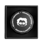 En sort hexagonal grinder med en diameter på 55 mm. Overfladen er mat og ensartet, uden synlige reflekser. Kanten er let afrundet, hvilket giver en blødere profil. Der er indgraverede linjer langs kanten, der skaber et geometrisk mønster. Grinderens indre har skarpe tænder, der er synlige, og en fin struktur, der sikrer effektiv kværning.