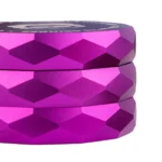 En lilla, hexagonal grinder med en diameter på 55 mm. Overfladen har en glat, mat tekstur, mens kanten er let afrundet. Der ses fine mønstre på toppen, og indvendigt er der skarpe tænder til at male. Grinden har en enkel lukning og en lille skrift på siden, som angiver producentens navn.