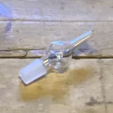 Mundstykket er fremstillet af klart glas og præsenterer en glat, gennemsigtig overflade. Det har en cylindrisk form med en let afrundet spids, der tilføjer en subtil elegance. Kanten er skarpt defineret, mens der er let buede former nær bunden. Ingen synlige dekorationer eller mønstre findes, hvilket giver et minimalistisk udtryk.