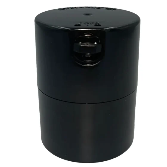 En sort, cylindrisk beholder med en glat overflade og en skinnende finish. Låget er fladt og har en let skridsikker struktur. Beholderen har en kapacitet på 290 ml og prydes af et minimalistisk design uden synlige knapper eller symboler. Den er fremstillet af plastmateriale, der giver en robust og holdbar fornemmelse.
