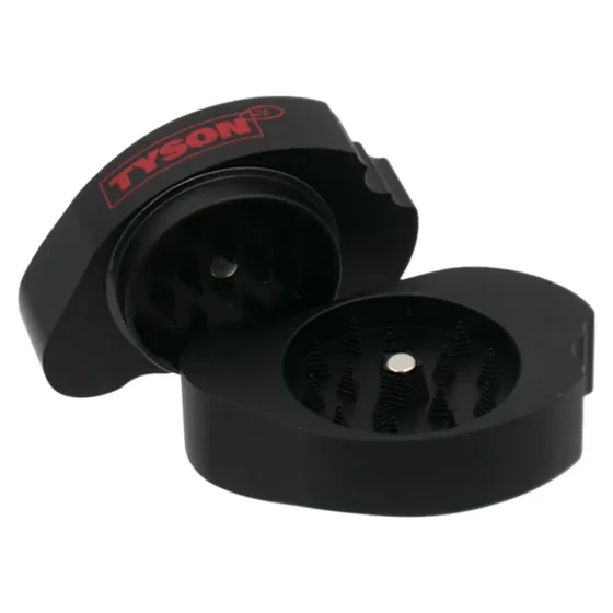 En sort metal grinder præsenteres med en mat overflade og en slank, cylindrisk form. Øverste del har en skridsikker tekstur for bedre greb, mens den nederste del er udstyret med en skarp tandstruktur til formaling. Der er små ventilationshuller langs kanten, og en diskret logoindgravering pryder overfladen, hvilket tilføjer et stilrent element.