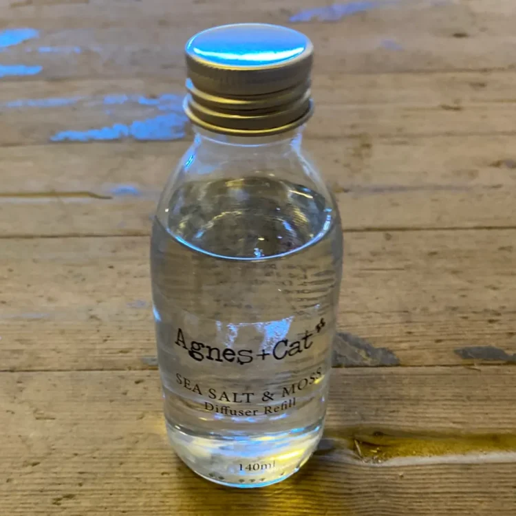 Agnes+Cat Sea Salt and Moss 140 ml (Fejl), klar glasflaske med klar væske og guldfarvet skruelåg. "Agnes+Cat" trykt i sort.