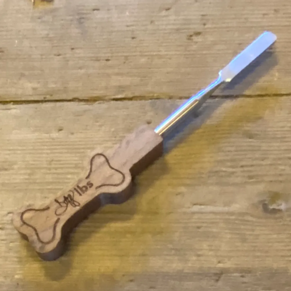 Dogg LBS Dabbing Kit med en smal, sølvfarvet metalspatel med afrundet ende på et brunt, kødbenformet træhåndtag.