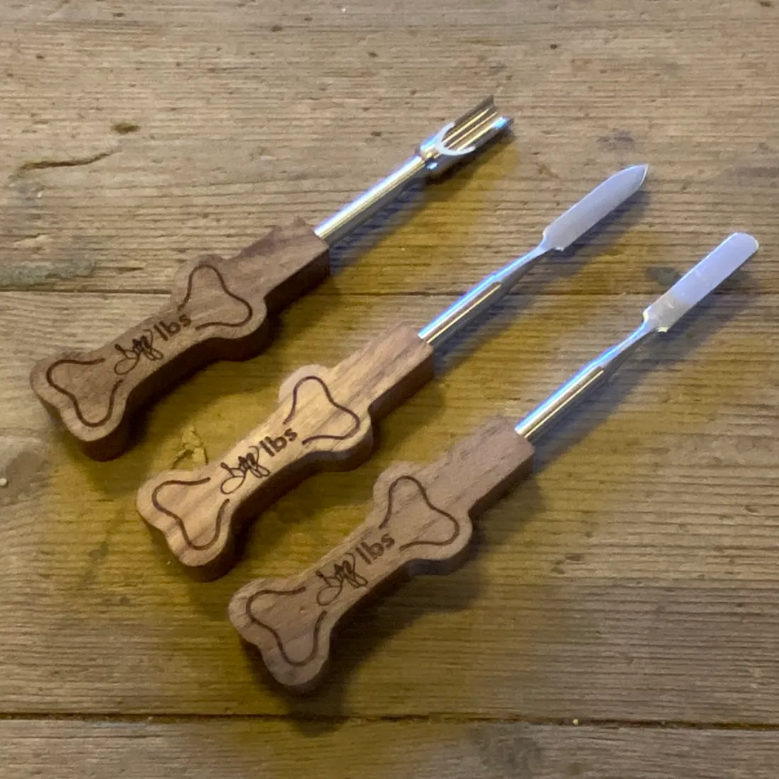 Dogg LBS Dabbing Kit med tre sølvfarvede metalredskaber og brune træhåndtag udskåret som kødben med mørk gravering.