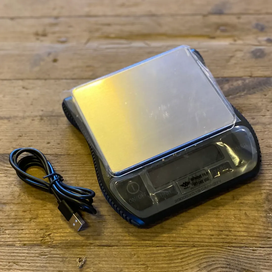 MyWeigh Barista Vægt 0,1-3000g med sølvfarvet metalplade over sort bund med display. Sort USB-kabel ved siden af.