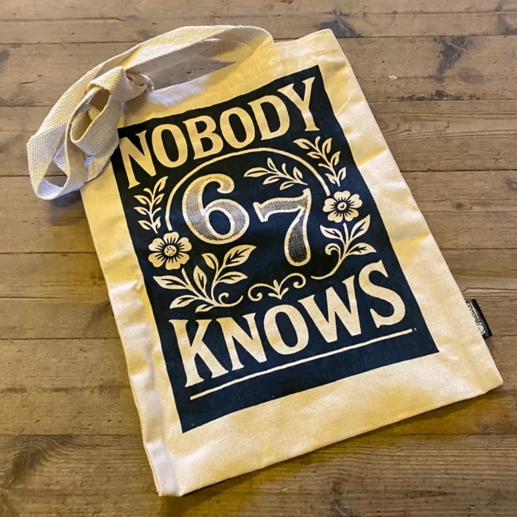 Nobody Knows Tote Bag m. Lynlås 32x42 cm i beige stof med sort trykfelt, blomster og teksten "NOBODY KNOWS".