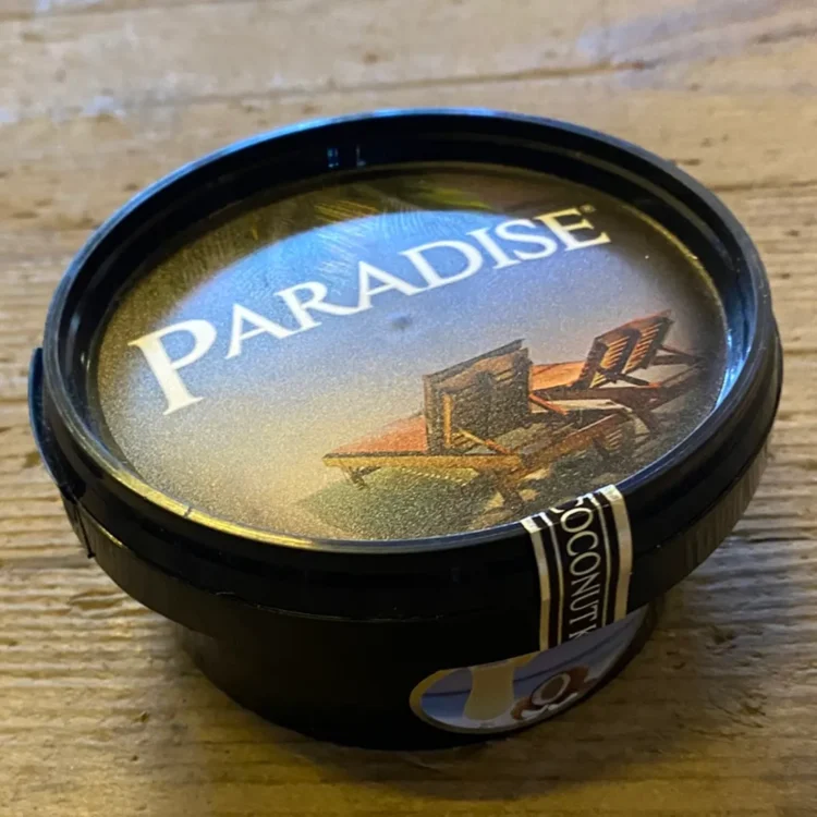 Paradise Coconut Kiss Steam Stones 120g i sort bøtte med liggestole på lågets etiket og "PARADISE" trykt i hvidt.