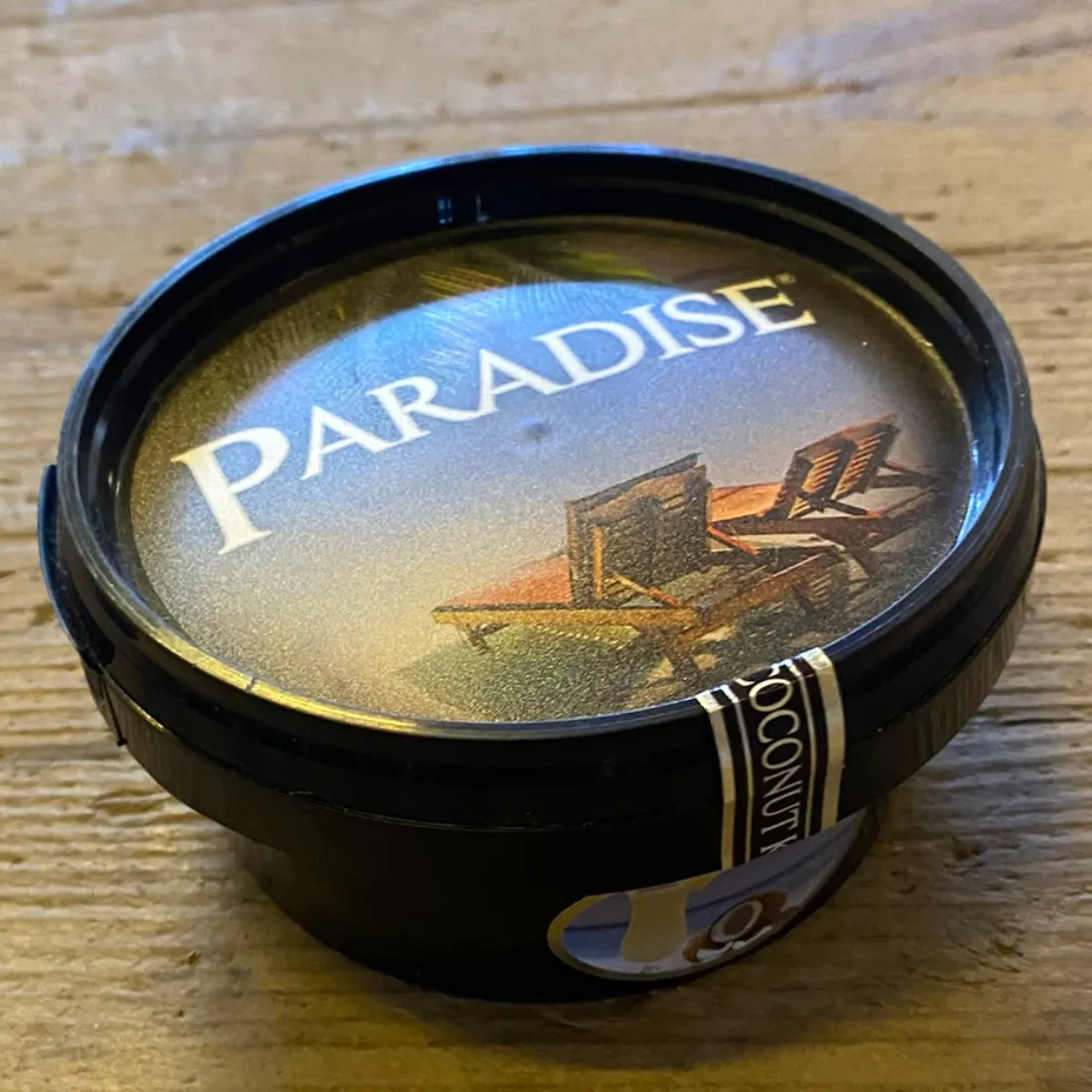 Paradise Coconut Kiss Steam Stones 120g i sort bøtte med liggestole på lågets etiket og "PARADISE" trykt i hvidt.